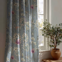 Close-up of white dandelion clocks and pink wildflowers on dusty blue curtain fabric