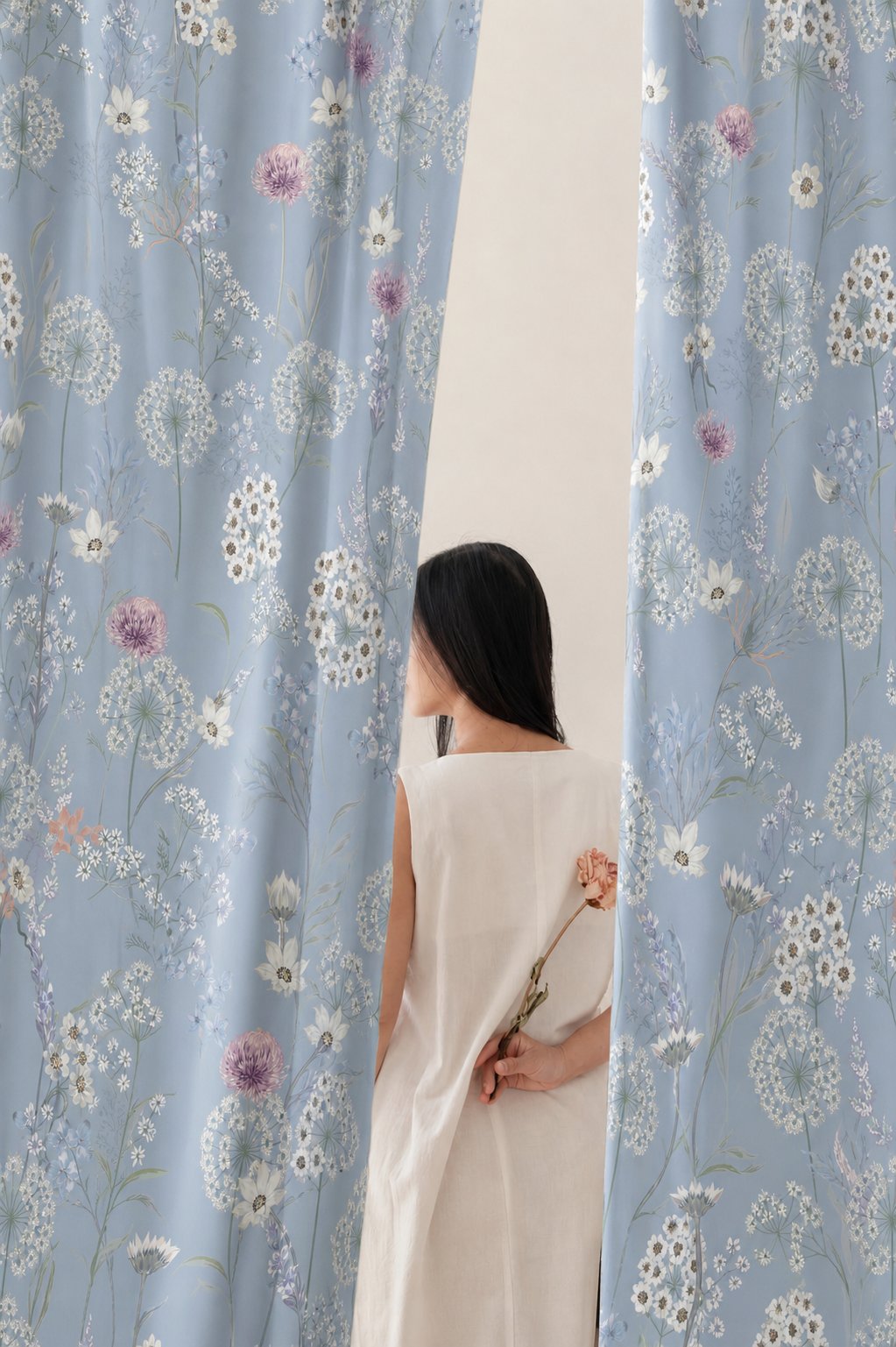 Woman standing between two blue dandelion print curtain panels