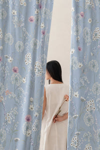 Woman standing between two blue dandelion print curtain panels