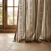 Hem of a green and rust painted stripe curtain resting on a stone floor