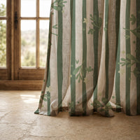 Hem of a green stripe botanical sprig curtain resting on a stone floor