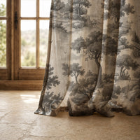 Hem of a grey landscape toile curtain resting on a stone floor