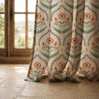 Hem of a orange ogee floral curtain resting on a stone floor