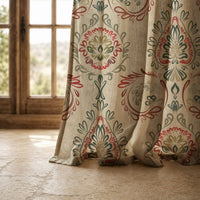 Hem of a red and green folk damask curtain resting on a stone floor