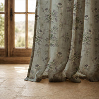 Hem of a sage blue vintage rose curtain resting on a stone floor