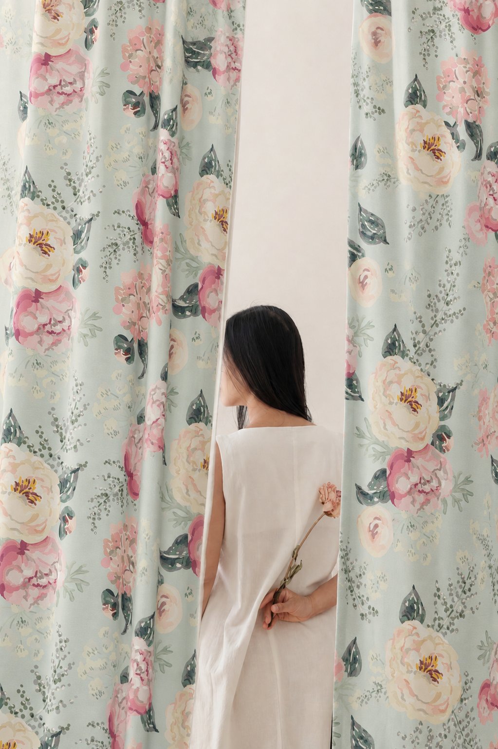 Woman standing between two sage green peony floral curtain panels