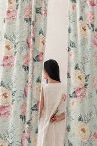 Woman standing between two sage green peony floral curtain panels