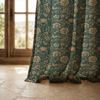 Hem of a teal arts and crafts floral curtain resting on a stone floor